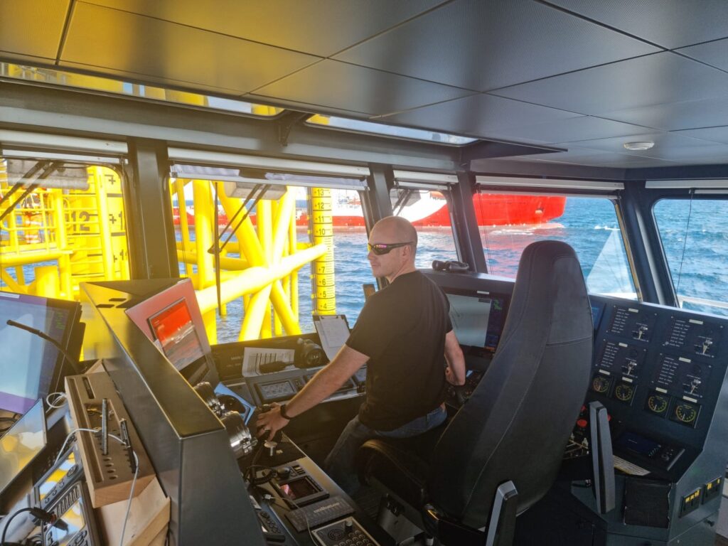 Captain Scott Campbell at the helm during CTV ops, at an offshore renewable energy substation. SIMOPS in the backgorund.